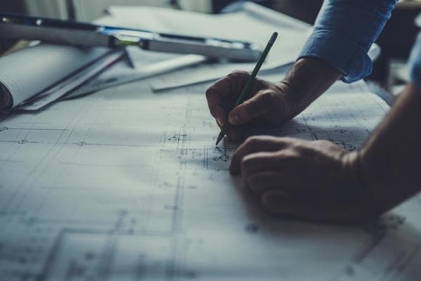 An architect is seen writing on blueprints laid out on top of a table next to a level.